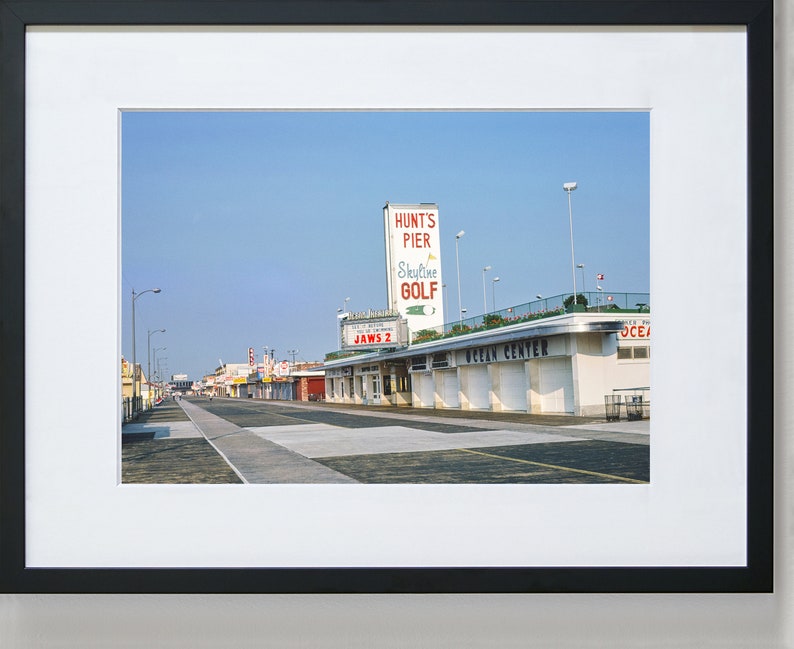 May include: A vintage photograph of a boardwalk with a sign for Hunt's Pier Skyline Golf and a building labelled "Ocean Centre".