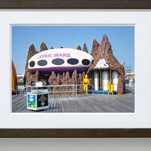 May include: A vintage Star Wars themed amusement park ride with a purple and white spaceship, brown rock formations, and yellow figures of C-3PO and R2-D2.