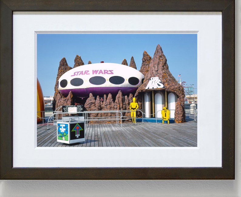 May include: A vintage Star Wars themed amusement park ride with a purple and white spaceship, brown rock formations, and yellow figures of C-3PO and R2-D2.