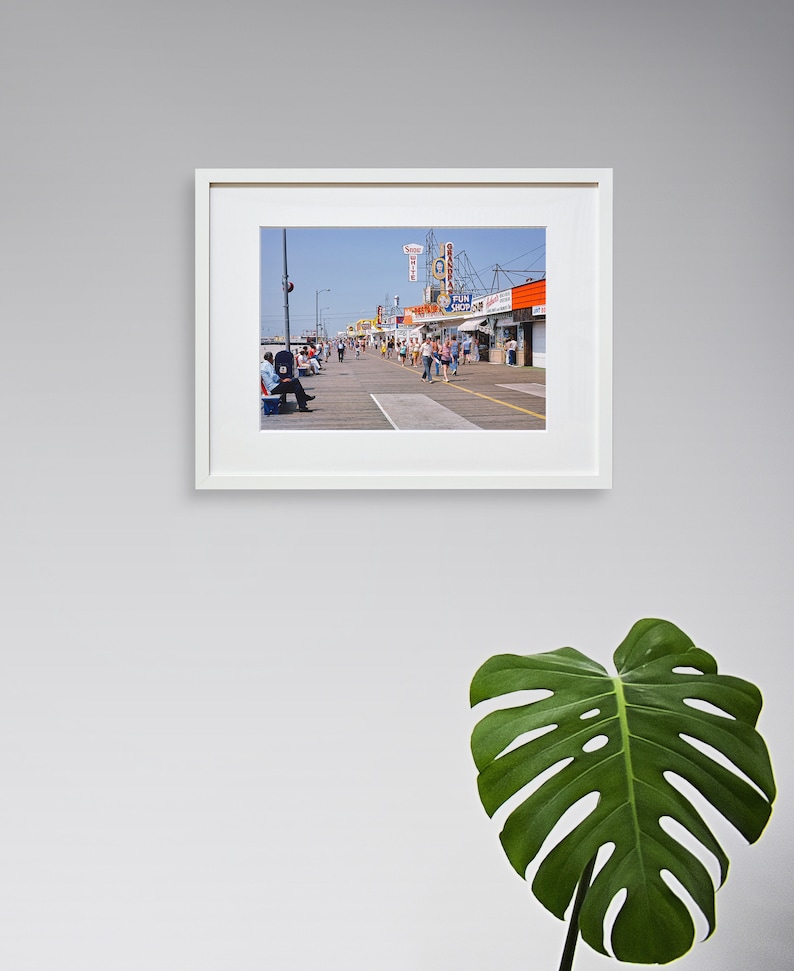Peut inclure: Une photographie encadr&eacute;e d'une promenade avec des gens qui marchent et des boutiques de chaque c&ocirc;t&eacute;. Les boutiques ont des enseignes color&eacute;es avec du texte comme "Salute" et "Fun Center".