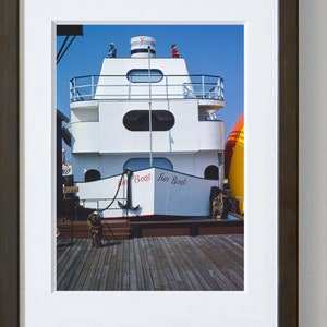May include: A white boat with red and blue accents, docked at a pier. The boat has a large anchor hanging from the front and the words "Fun Boat" written on the side.