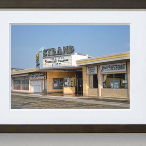 K&ouml;nnte beinhalten: Ein Vintage-Foto eines Kinos namens "The Strand" mit einem Leuchtkasten, der "Sylvester Stallone Fist" um 19:25 und 22:00 Uhr bewirbt.  Nebenan befindet sich ein Restaurant namens "Spire's Restaurant".