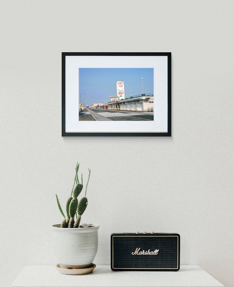 May include: A black and white photograph of a building with a sign that reads "Runt's Pier, Bathing, Golf". The building is situated on a street with a few cars parked in front of it.
