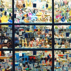 May include: A shop window display packed with a variety of items for sale, including jewellery, trinkets, and small toys. The window is divided into sections, each displaying a different selection of goods. Numerous price tags are visible, indicating the items are available to buy.