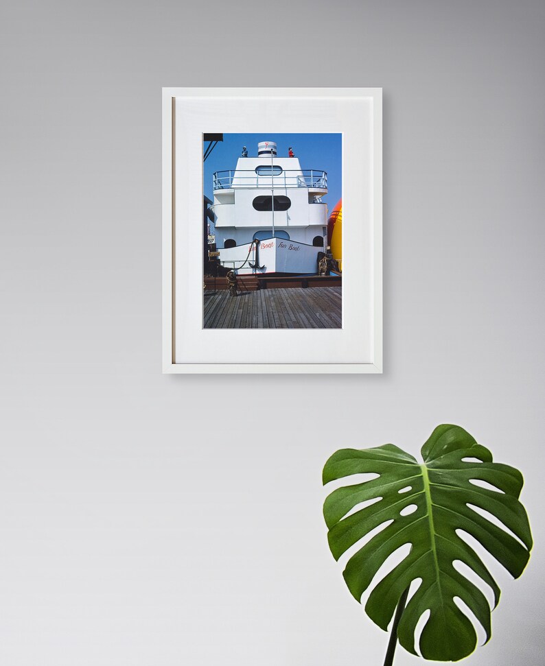 May include: A framed photograph of a white boat docked at a pier. The boat has a white cabin with a red and white sign that reads "Sea Boat".