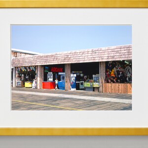 Pode incluir: Uma loja de arcade bem iluminada com uma placa vermelha que diz "ARCADE" e uma variedade de jogos de arcade vis&iacute;veis atrav&eacute;s das janelas. A loja &eacute; feita de madeira e tijolo e tem um toldo de madeira.