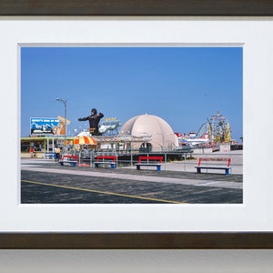 Op de afbeelding: Een vintage foto van een pretpark aan een boulevard met een groot gorillabeeld, een wit koepelvormig gebouw en een achtbaan op de achtergrond. De foto is gemaakt op een zonnige dag met een blauwe lucht.