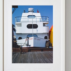 May include: A white boat with a red and blue striped roof and the words "Fun Boat" written on the side. The boat is docked at a wooden pier.