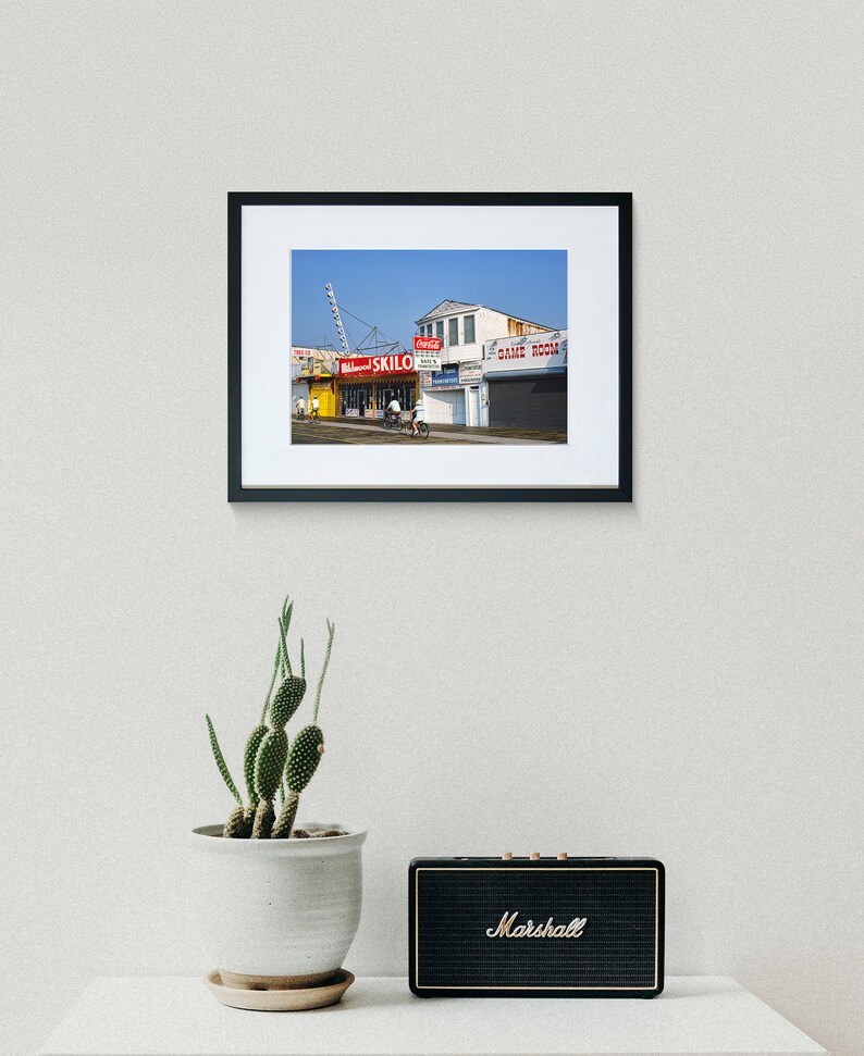 May include: A framed photograph of a colorful building with a red sign that reads "Skilo's" and a blue sign that reads "Game Room". The building is located on a street with a blue sky in the background.