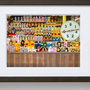 May include: A wall filled with colorful stuffed animals, including bears, bunnies, and other creatures. A large clock with black numbers on a white face is mounted on the wall. The clock reads 6:00.