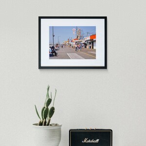 Peut inclure: Une photographie vintage d'une promenade avec des boutiques et des gens qui marchent. Les boutiques ont des enseignes avec les mots "Fun City" et "Toy Shop".