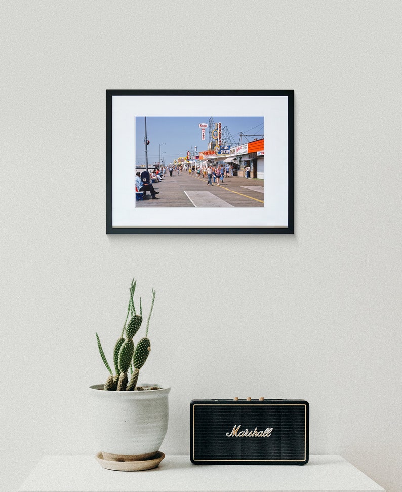 Peut inclure: Une photographie vintage d'une promenade avec des boutiques et des gens qui marchent. Les boutiques ont des enseignes avec les mots "Fun City" et "Toy Shop".