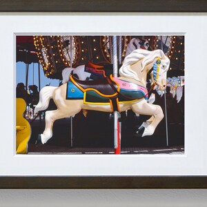 May include: A white carousel horse with a brown saddle, green, blue, and pink accents, and a gold bridle. The horse is in motion, with its legs raised in the air.