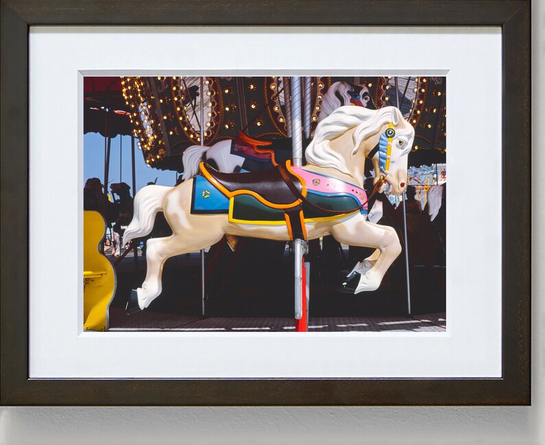 May include: A white carousel horse with a brown saddle, green, blue, and pink accents, and a gold bridle. The horse is in motion, with its legs raised in the air.