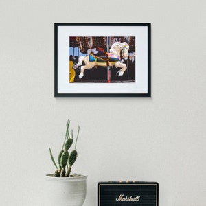 May include: A white carousel horse with a blue and yellow saddle, set against a dark background with twinkling lights.