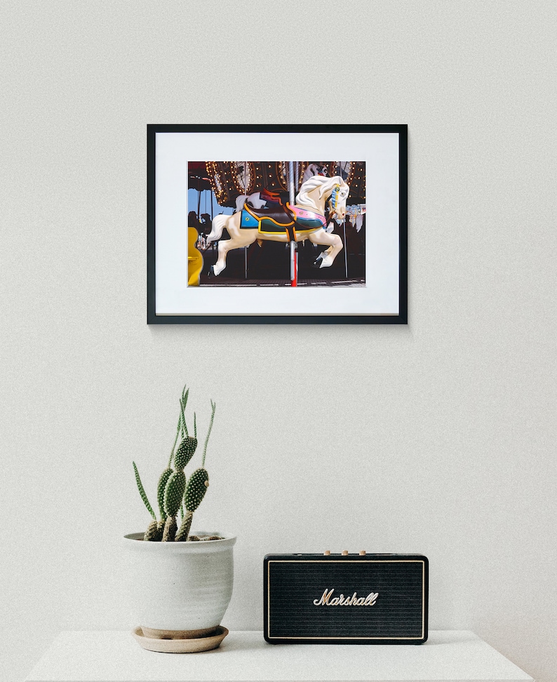 May include: A white carousel horse with a blue and yellow saddle, set against a dark background with twinkling lights.