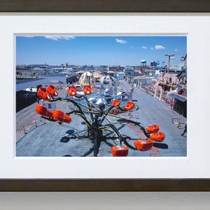 May include: A vintage amusement park ride with orange seats on a wooden boardwalk. The ride is in the shape of a spider with long arms and is surrounded by other rides and buildings.