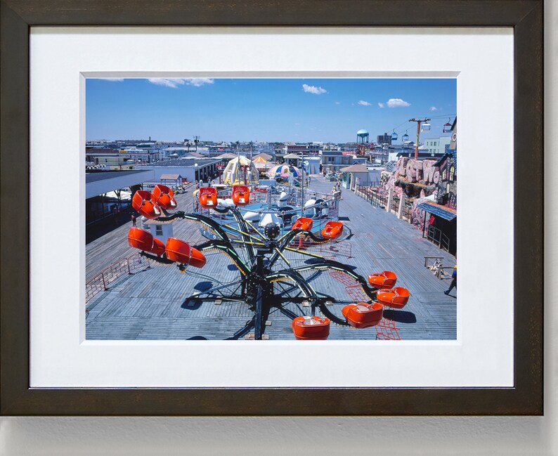 May include: A vintage amusement park ride with orange seats on a wooden boardwalk. The ride is in the shape of a spider with long arms and is surrounded by other rides and buildings.