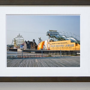 May include: A yellow and green sign with the text "Morey's Pier Presents... Bear Country Jubilee" on a boardwalk with a roller coaster and other amusement park rides in the background.