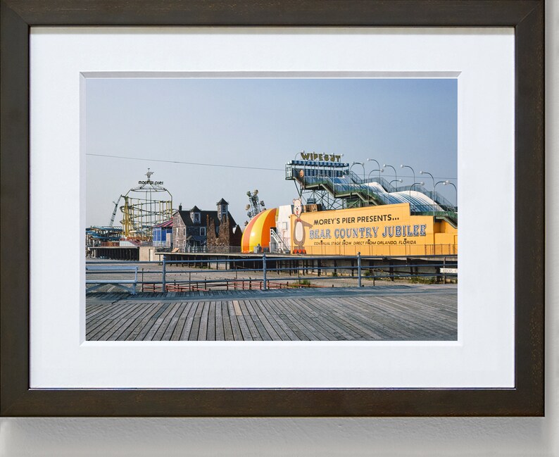 May include: A yellow and green sign with the text "Morey's Pier Presents... Bear Country Jubilee" on a boardwalk with a roller coaster and other amusement park rides in the background.