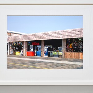 Pode incluir: Uma loja de arcade bem iluminada com uma placa vermelha que diz "ARCADE" e uma variedade de jogos de arcade vis&iacute;veis atrav&eacute;s das janelas. A loja est&aacute; localizada em um cal&ccedil;ad&atilde;o de madeira.