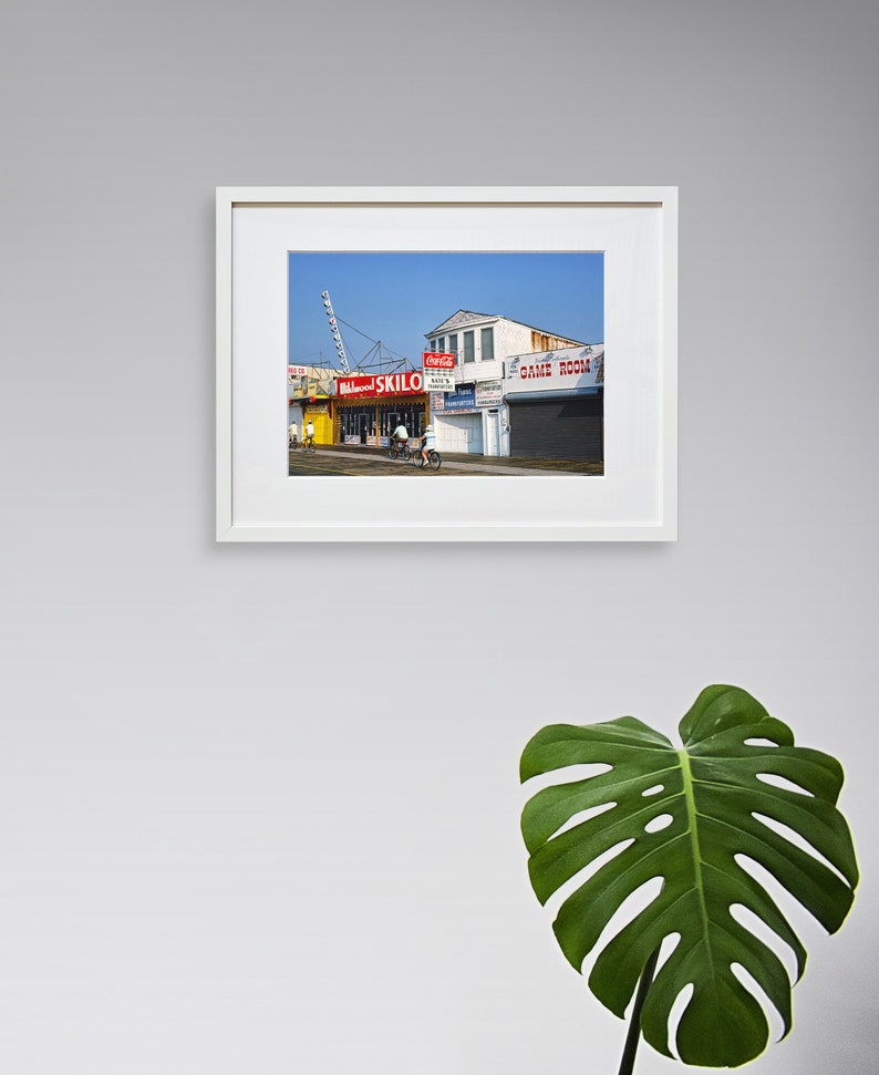 May include: A vintage photograph of a boardwalk scene with a Ferris wheel in the background. The photo shows a building with a sign that reads "Skillo" and another sign that reads "Game Room".