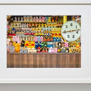 May include: A vintage carnival game with a large clock face and a wall of stuffed animals. The clock face has the numbers 3, 6, 1, 4, 5, and 2. The stuffed animals are mostly colorful and include bears, dogs, and other animals.