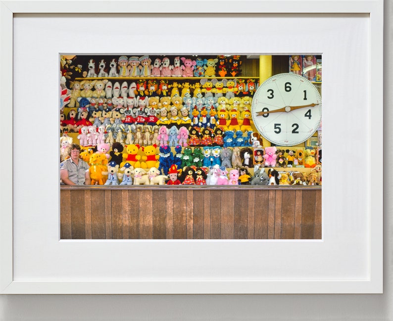 May include: A vintage carnival game with a large clock face and a wall of stuffed animals. The clock face has the numbers 3, 6, 1, 4, 5, and 2. The stuffed animals are mostly colorful and include bears, dogs, and other animals.