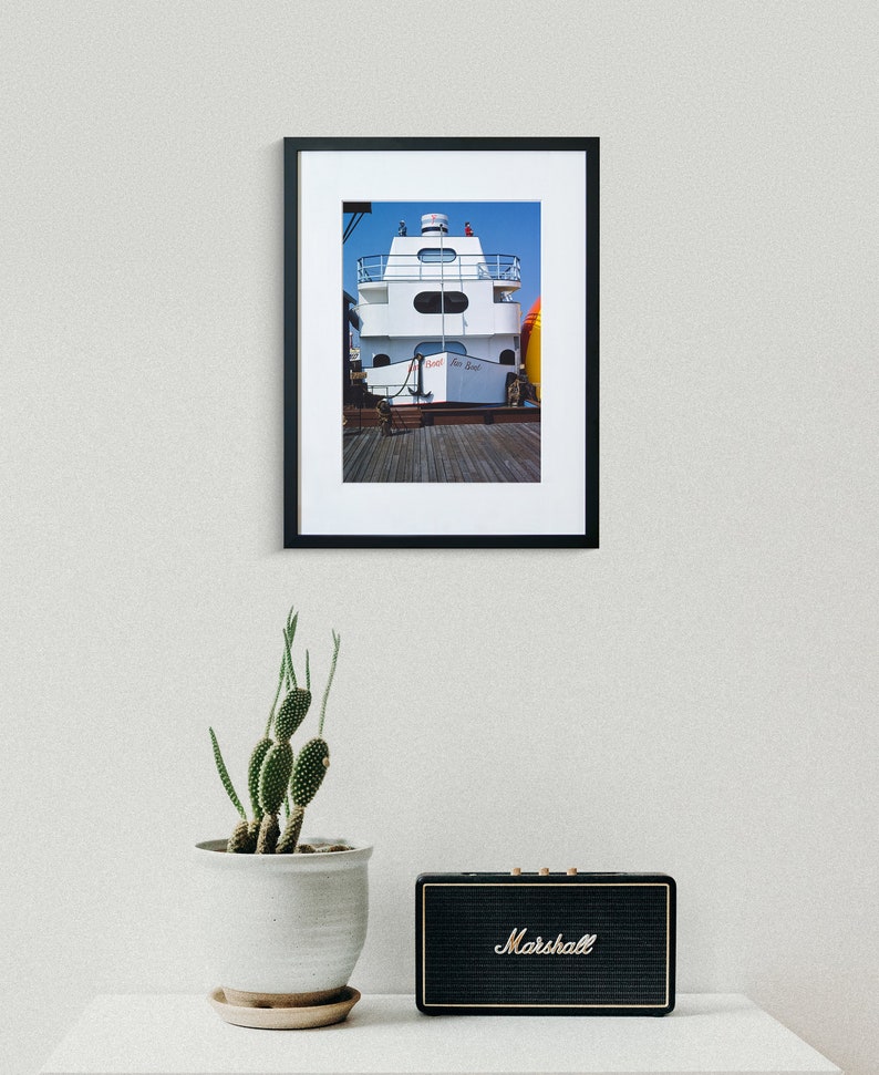 May include: A framed photograph of a white boat with a red and blue sign that says "Sunset River Boat". The boat is docked at a pier and there are people on the deck.
