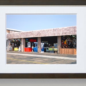 Pode incluir: Uma loja de arcade bem iluminada com uma marquise vermelha e azul. A arcade est&aacute; localizada em um cal&ccedil;ad&atilde;o e tem uma variedade de jogos e pr&ecirc;mios vis&iacute;veis atrav&eacute;s das janelas. A placa acima da entrada diz "ARCADE".
