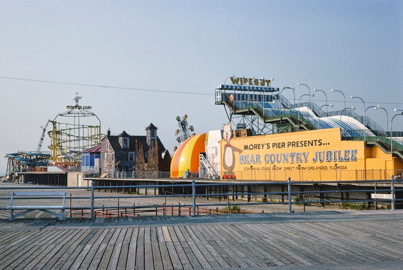 May include: A yellow and blue roller coaster with a sign that reads "Morey's Pier" in front of a yellow building with a sign that reads "Morey's Pier Presents... Bear Country Jubilee.  Annual Stage Show Direct From Orlando, Florida."
