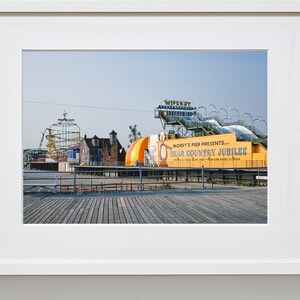 May include: A yellow and white sign with the text "Morey's Pier Presents... Bear Country Jubilee" on a boardwalk with a roller coaster and other amusement park rides in the background.
