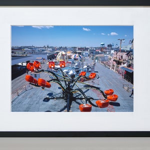 May include: A vintage photograph of a carnival ride with orange seats on a wooden boardwalk. The ride is a spinning octopus with long arms. The photo was taken from above, looking down on the ride.