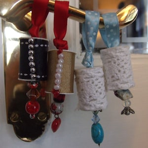 Pode incluir: Quatro porta-chaves decorativos com estilos diferentes. O primeiro é preto com costuras brancas e contas prateadas, o segundo é dourado com contas brancas, o terceiro e o quarto são de renda branca com fita de bolinhas azuis.