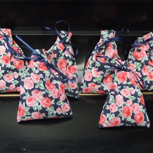 Puede incluir: Seis pequeñas bolsas de tela con fondo azul marino y estampados florales rosas. Las bolsas tienen lazos de cinta azul marino.