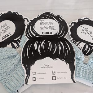 May include: Three handmade crocheted ear warmers in light blue, each with a decorative rhinestone band. The ear warmers are labeled for Adult, Child, and Toddler sizes. The black and white tags include care instructions.