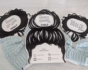 May include: Three handmade crocheted ear warmers in light blue, each with a decorative rhinestone band. The ear warmers are labeled for Adult, Child, and Toddler sizes. The black and white tags include care instructions.