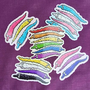 May include: A set of 12 colorful worm stickers. The stickers are in various colors, including red, orange, yellow, green, blue, purple, and pink. Each sticker features a worm with a smiling face and a fuzzy texture.