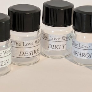 Pode incluir: Cinco pequenos frascos de vidro com tampas pretas. Cada frasco tem um rótulo com o texto "The Love Witch" e uma palavra: QUEEN, DESIRE, DIRTY, APHRODI e JUICY. Os frascos estão dispostos sobre uma superfície clara.