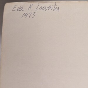 Op de afbeelding: Een close-up van een cr&egrave;mekleurig papier met handgeschreven tekst in blauwe inkt. De tekst luidt "Eva K. Laevastu 1973". Het papier heeft een licht verouderde uitstraling.