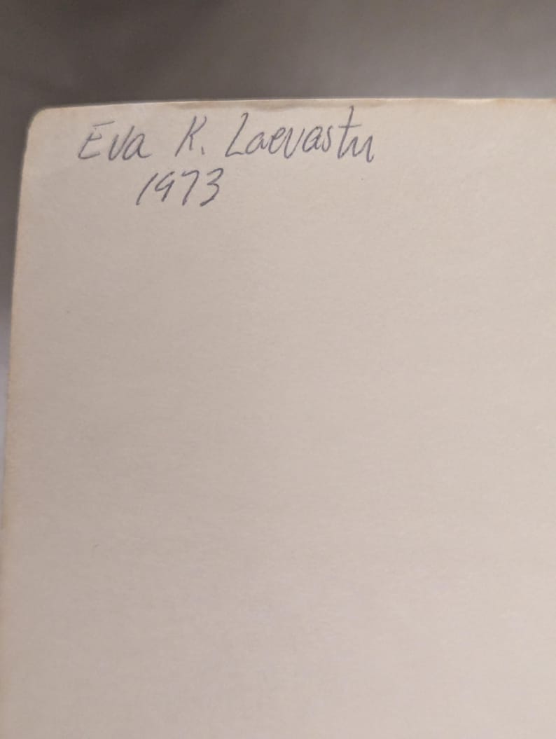 Op de afbeelding: Een close-up van een cr&egrave;mekleurig papier met handgeschreven tekst in blauwe inkt. De tekst luidt "Eva K. Laevastu 1973". Het papier heeft een licht verouderde uitstraling.
