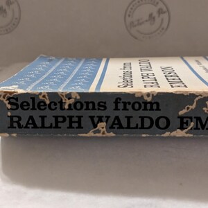 Op de afbeelding: Een vintage boek getiteld "Selections from Ralph Waldo Emerson". De rug is verbleekt blauw met witte strepen en tekst. De randen vertonen tekenen van slijtage, met de titel en de naam van de auteur duidelijk zichtbaar.