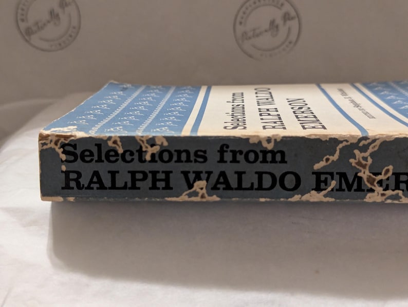 Op de afbeelding: Een vintage boek getiteld "Selections from Ralph Waldo Emerson". De rug is verbleekt blauw met witte strepen en tekst. De randen vertonen tekenen van slijtage, met de titel en de naam van de auteur duidelijk zichtbaar.