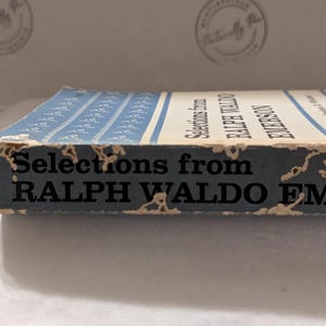 Op de afbeelding: Een vintage boek getiteld "Selections from Ralph Waldo Emerson". Het boek heeft een blauw-witte omslag met een patroon. De rug toont de titel en de naam van de auteur in zwarte tekst. De randen vertonen tekenen van slijtage.