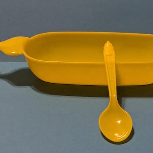 May include: A yellow plastic bowl with a handle and a matching yellow plastic spoon. The bowl is shaped like a boat.