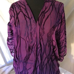 May include: A purple sheer top with a V-neck and a black and purple abstract pattern.