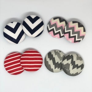 May include: Set of six fabric covered buttons with different geometric patterns. Two buttons feature a black and white chevron pattern, two buttons feature a pink, gray, and white chevron pattern, and two buttons feature a red and white striped pattern.