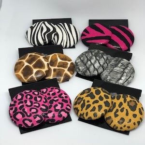 May include: A set of six pairs of round, fabric earrings. Each pair features a different animal print: zebra, pink and black zebra, giraffe, gray snake, pink leopard, and brown leopard.