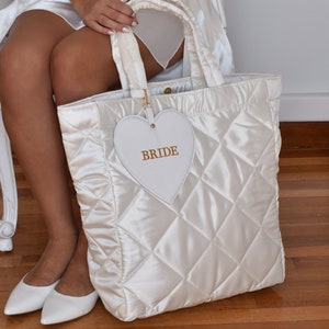 White quilted satin bridal tote bag with “Bride” detail, displayed with detachable zip pouch, elegant wedding accessory.
