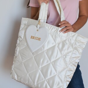 White bride tote bag in wedding preparation setting, quilted satin with pouch, perfect for wedding morning essentials.